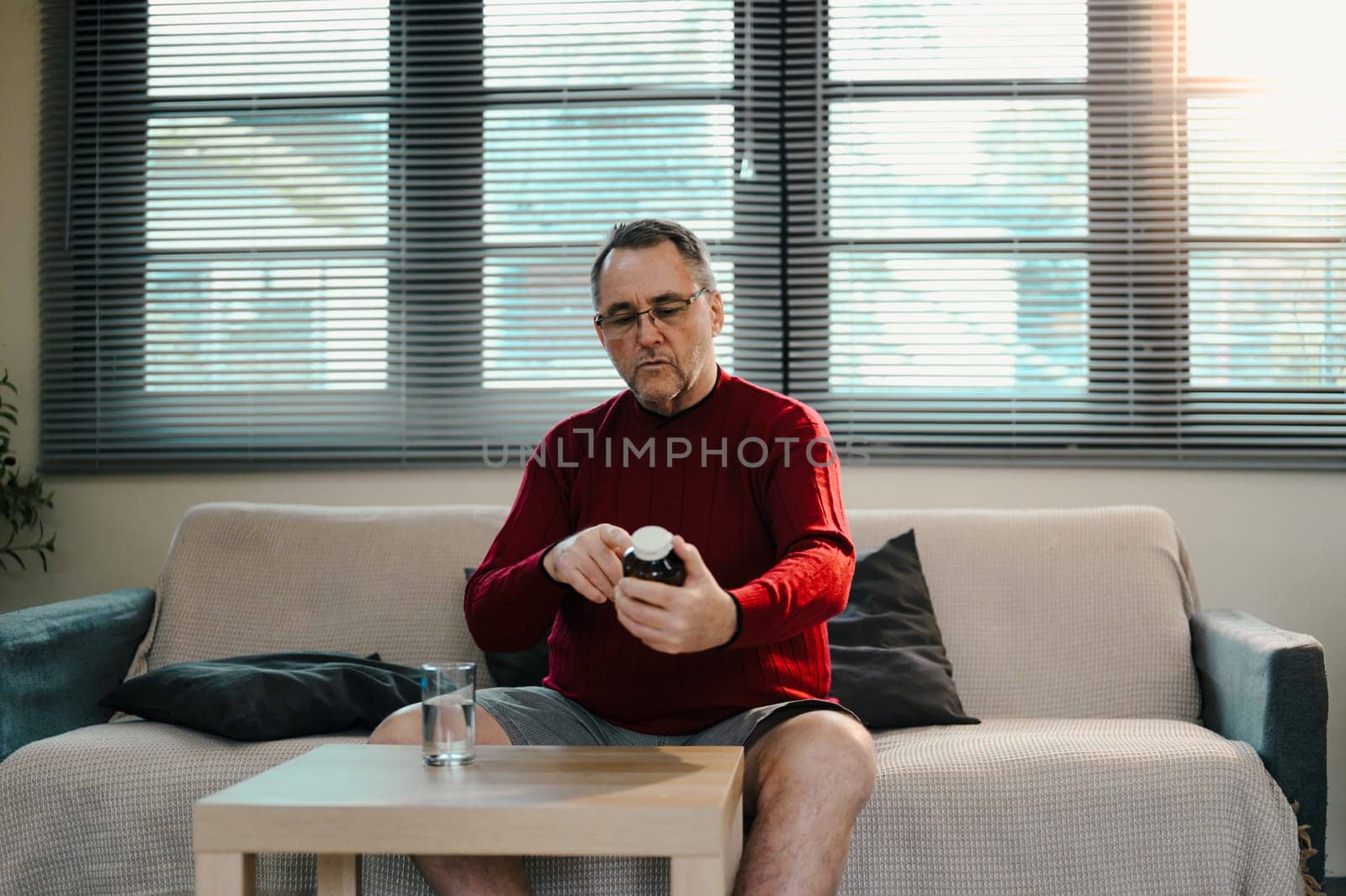 Mature man reviews the instructions on a bottle of pills with a glass of water on the table.