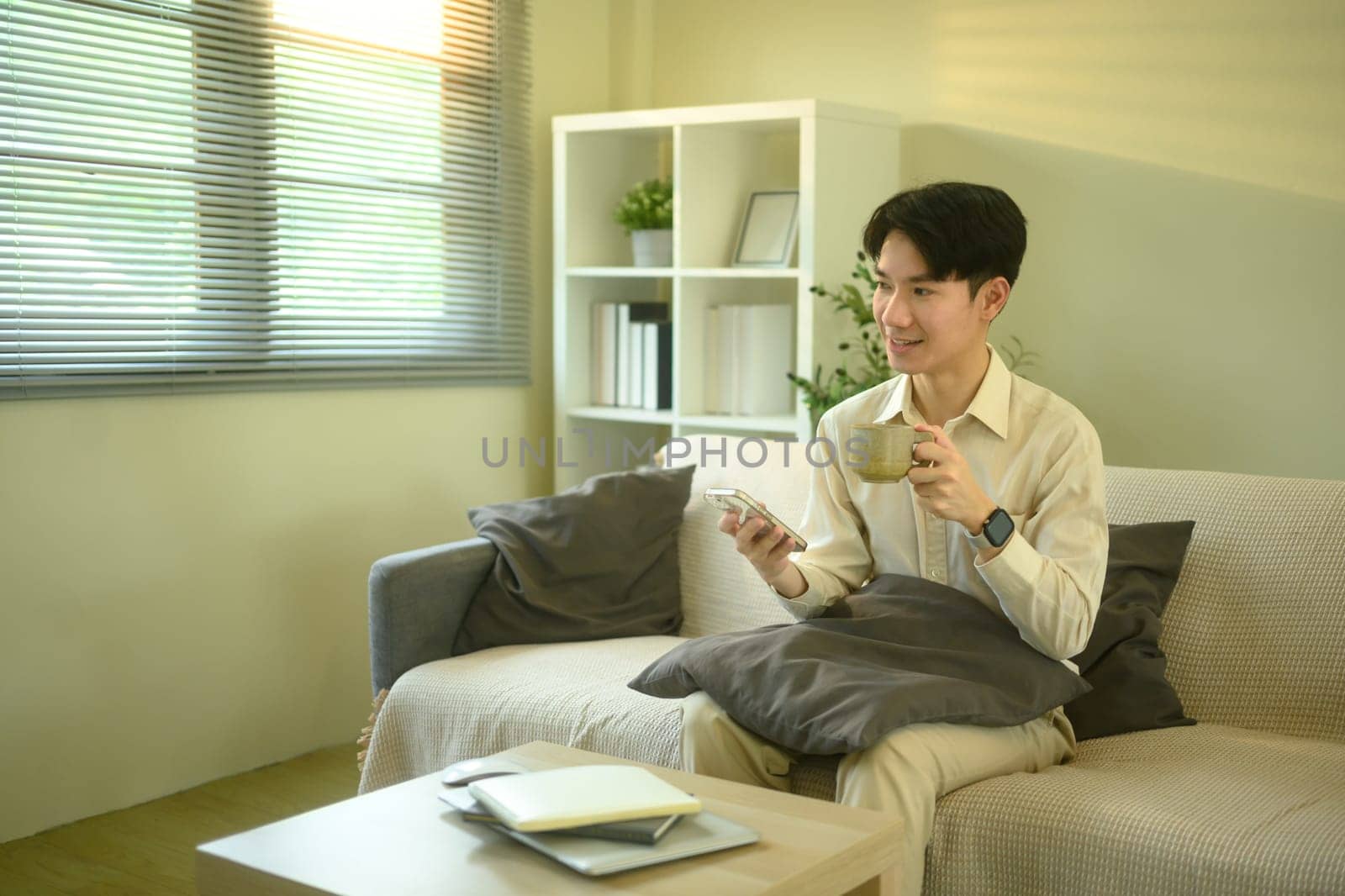 Smiling man checks messages or notifications on smartphone while seated in living room.