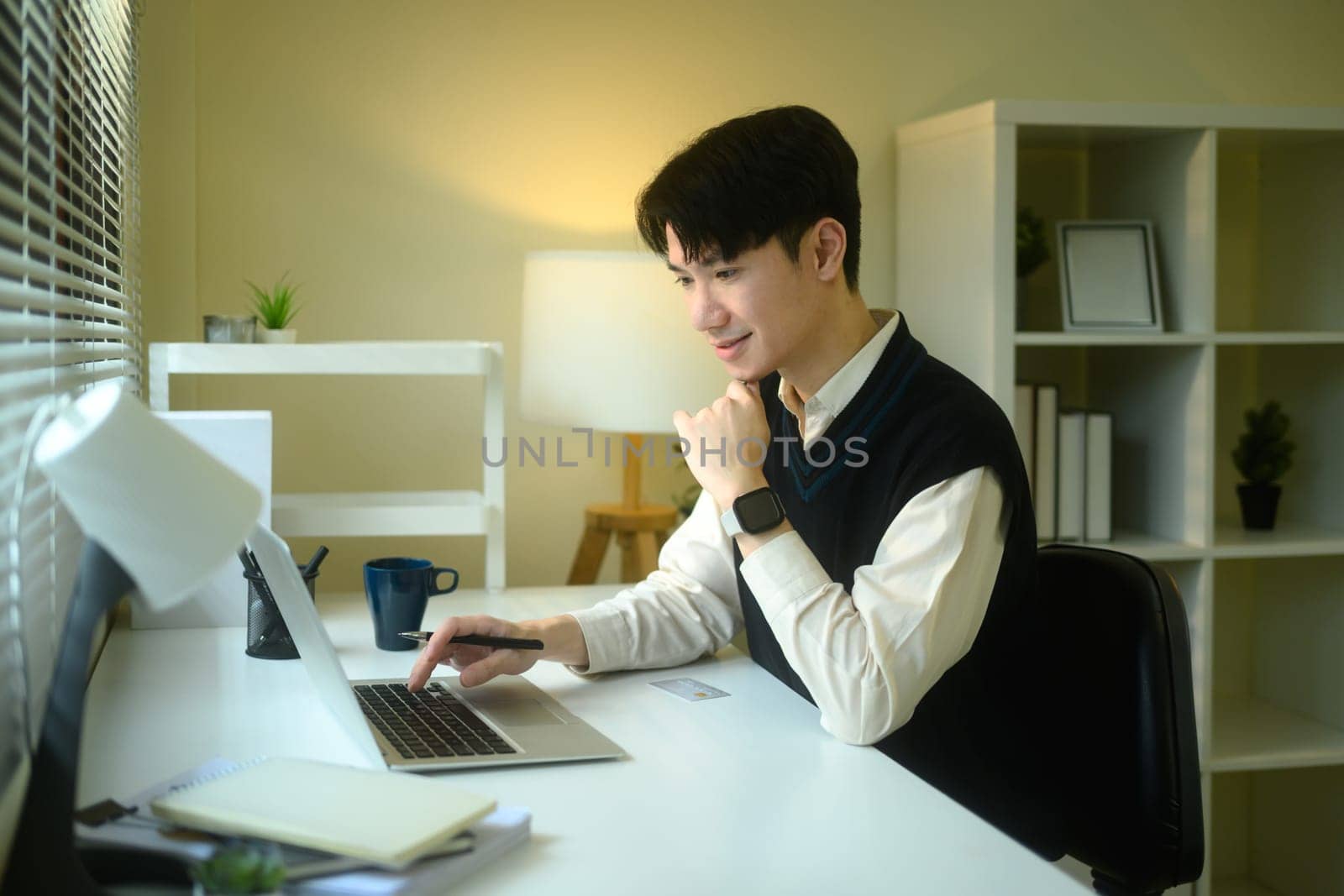 Young entrepreneur in a sweater vest uses a laptop at a minimalist desk.