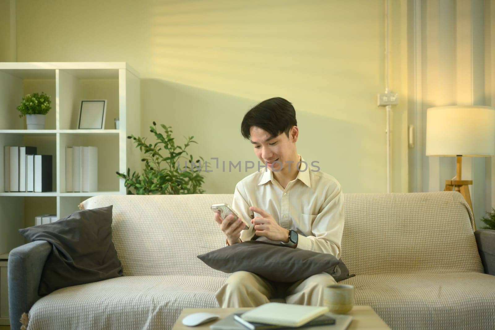 Smiling man checks messages or notifications on smartphone while seated in living room.