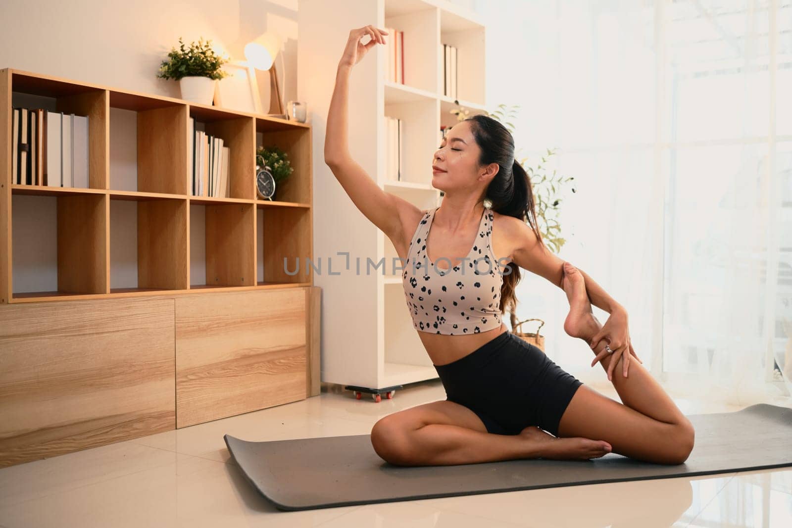Beautiful asian woman practicing elegant yoga stretches in a peaceful living room.