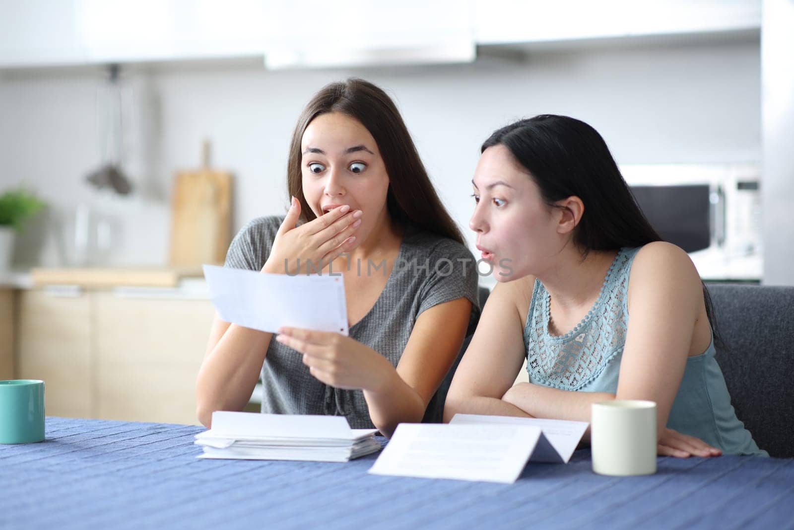 Amazed interracial women checking bank statement in the kitchen at home