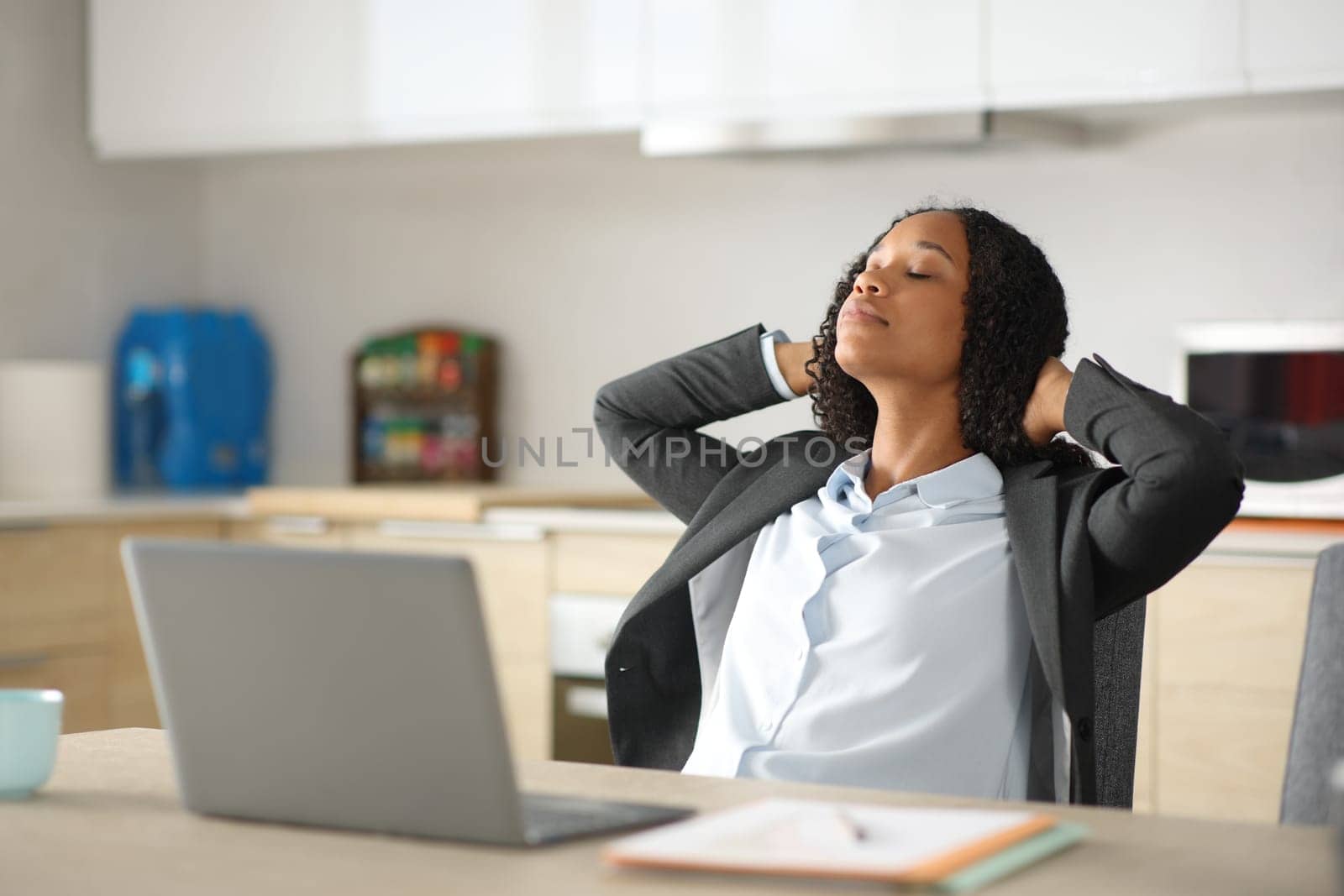 Black executive with laptop resting and relaxing in the kitchen at home