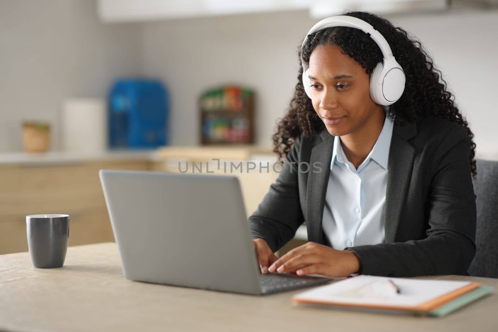 Black executive tele working with laptop and headphone in the kitchen at home
