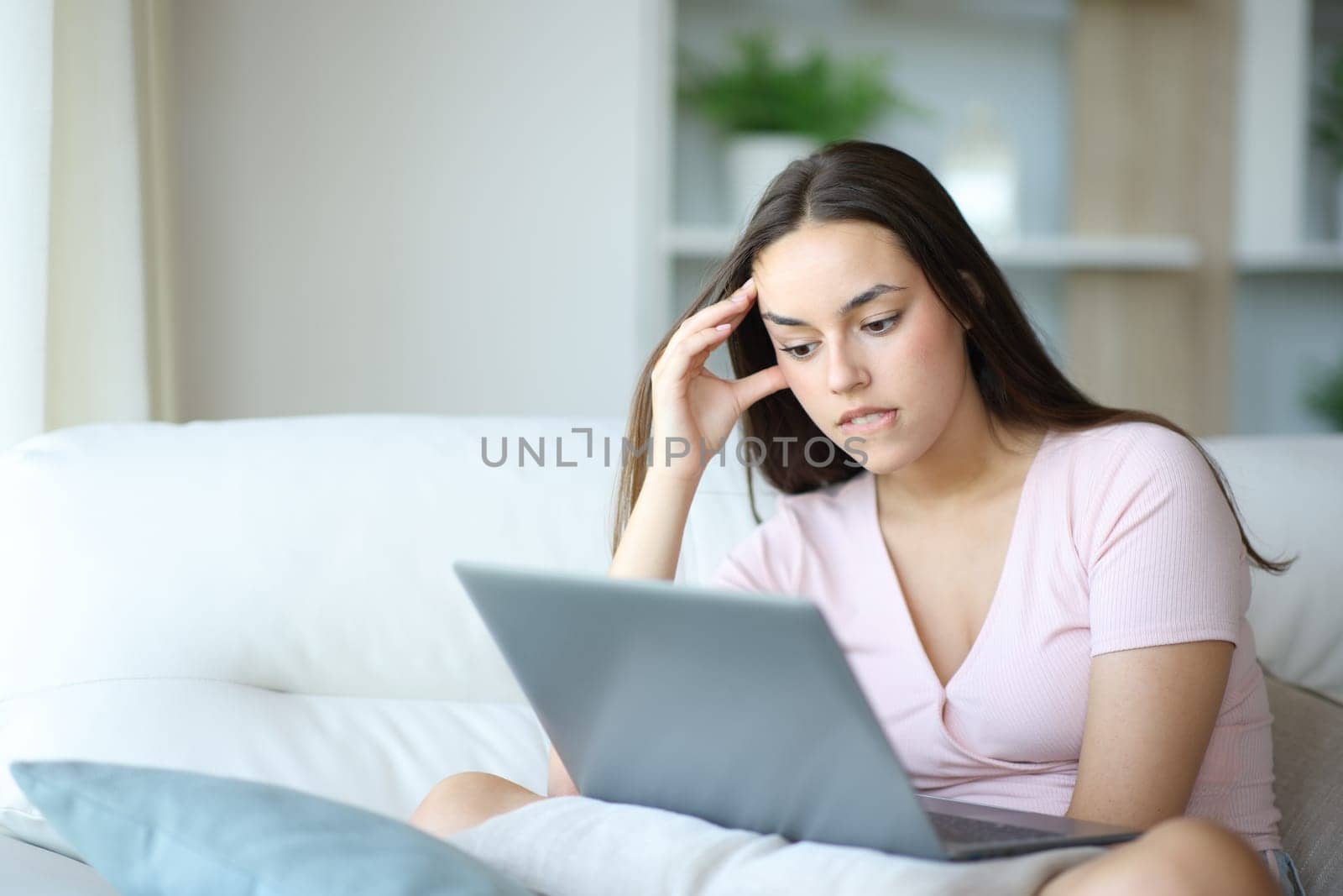 Frustrated woman complaining checking laptop after mistake sitting on a couch at home