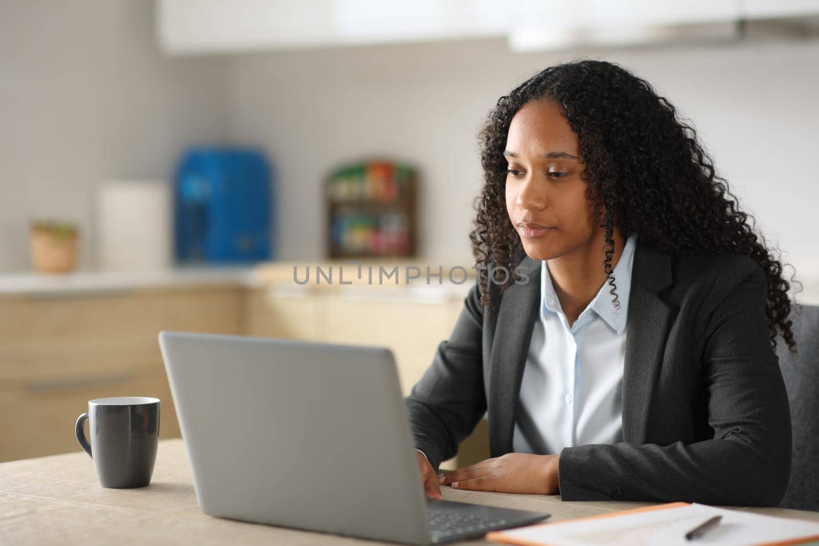 Serious black executive working online with laptop in the kitchen at home