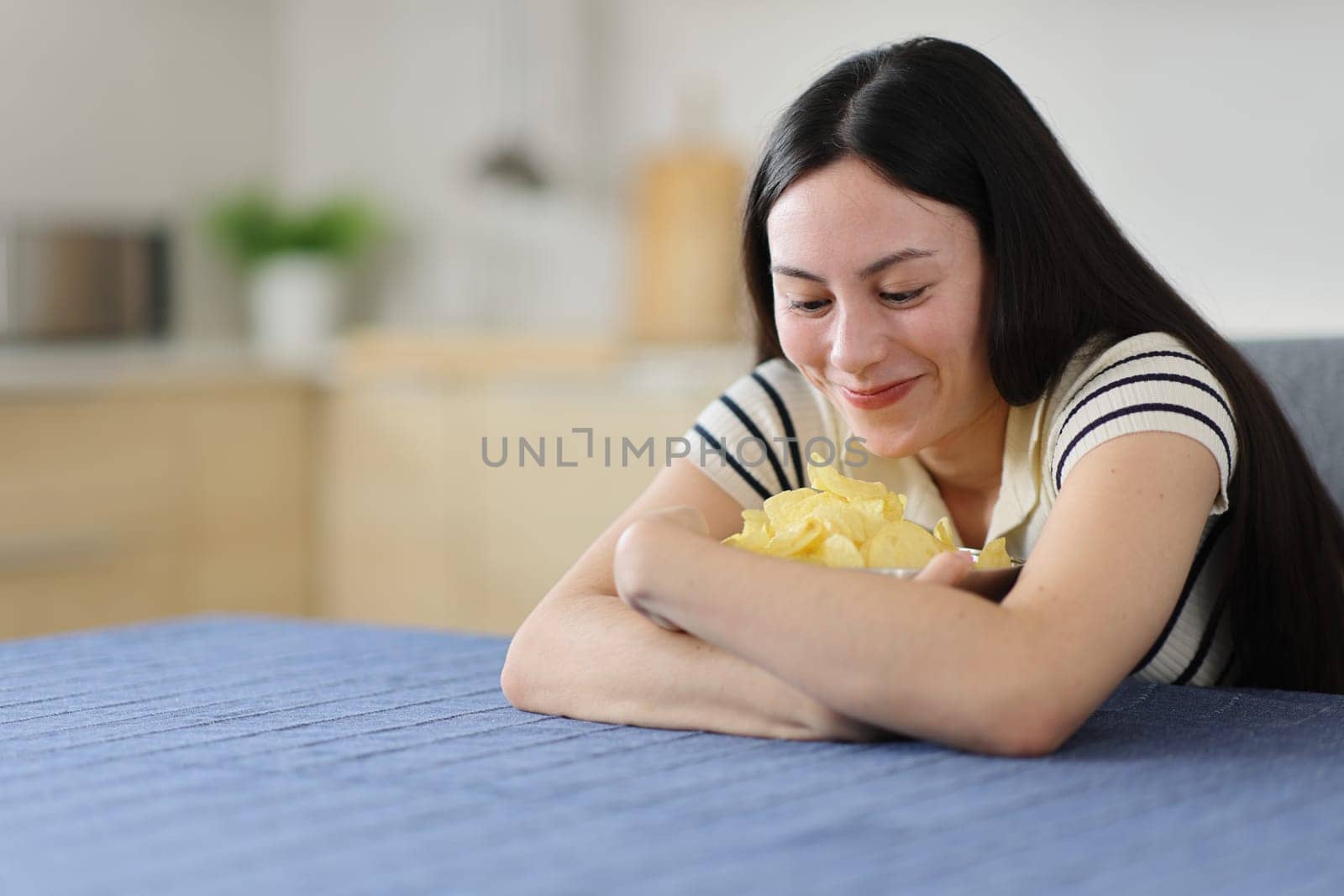 Gluttonous asian woman hugging potato chips in the kitchen at home