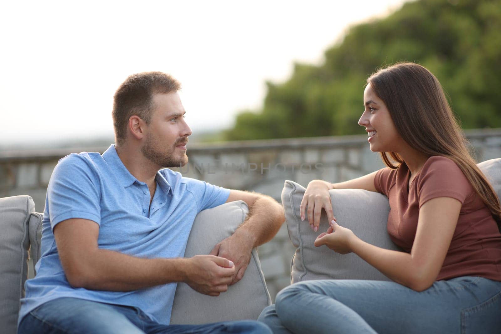 Couple or freinds talking sitting in a couch in a terrace at home