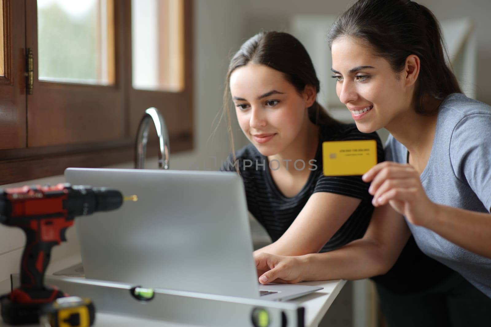 Couple reforming house buying online with credit card and laprop in the kitchen