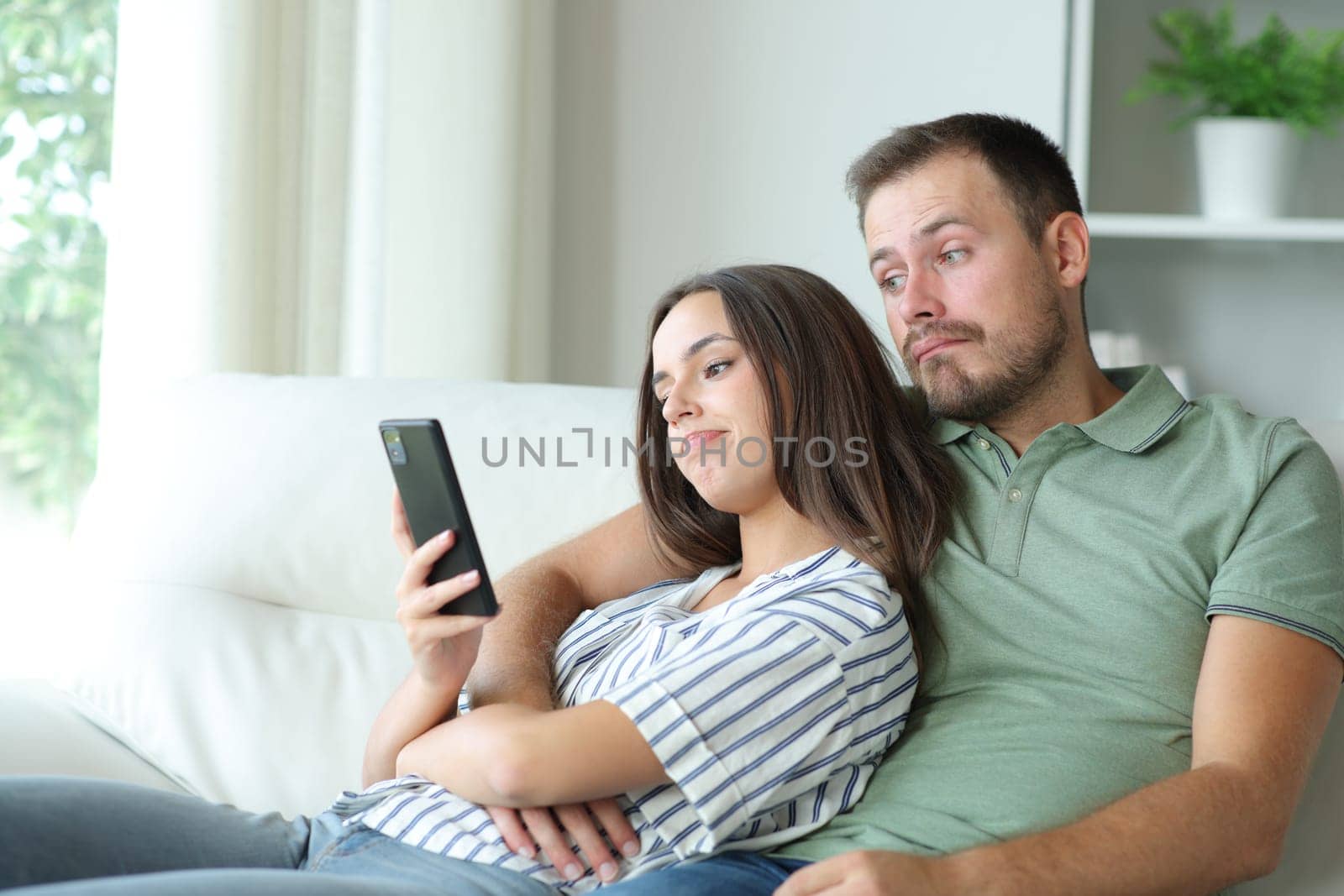 Disappointed couple checking boring phone online content sitting on a couch at home