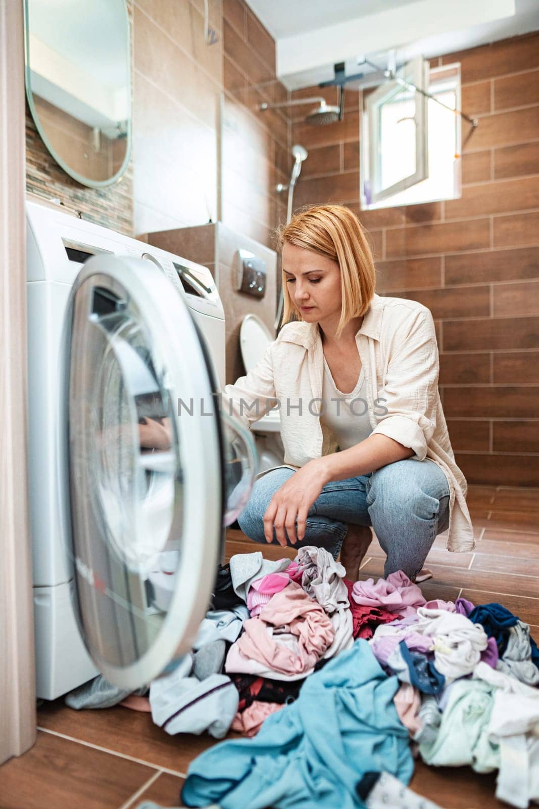 A woman sorts colorful clothes by a modern washing machine.