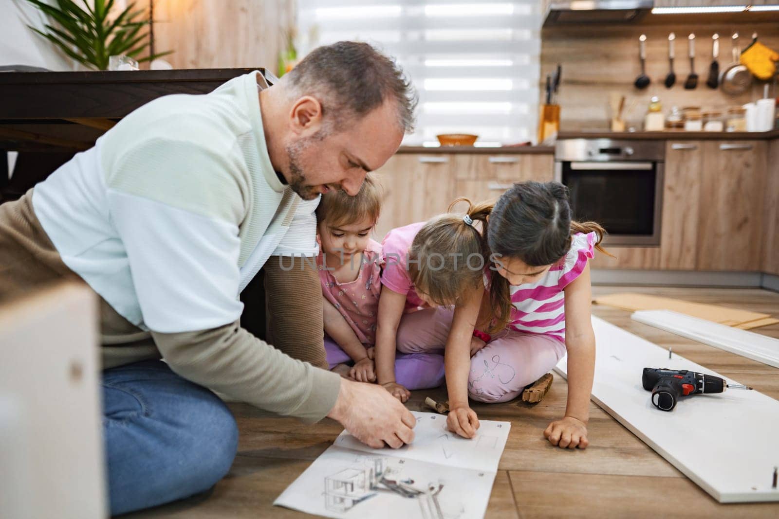 A father engages with his three daughters as they carefully examine instructions for a home project. The warm kitchen is filled with tools, laughter, and love on a sunny afternoon.