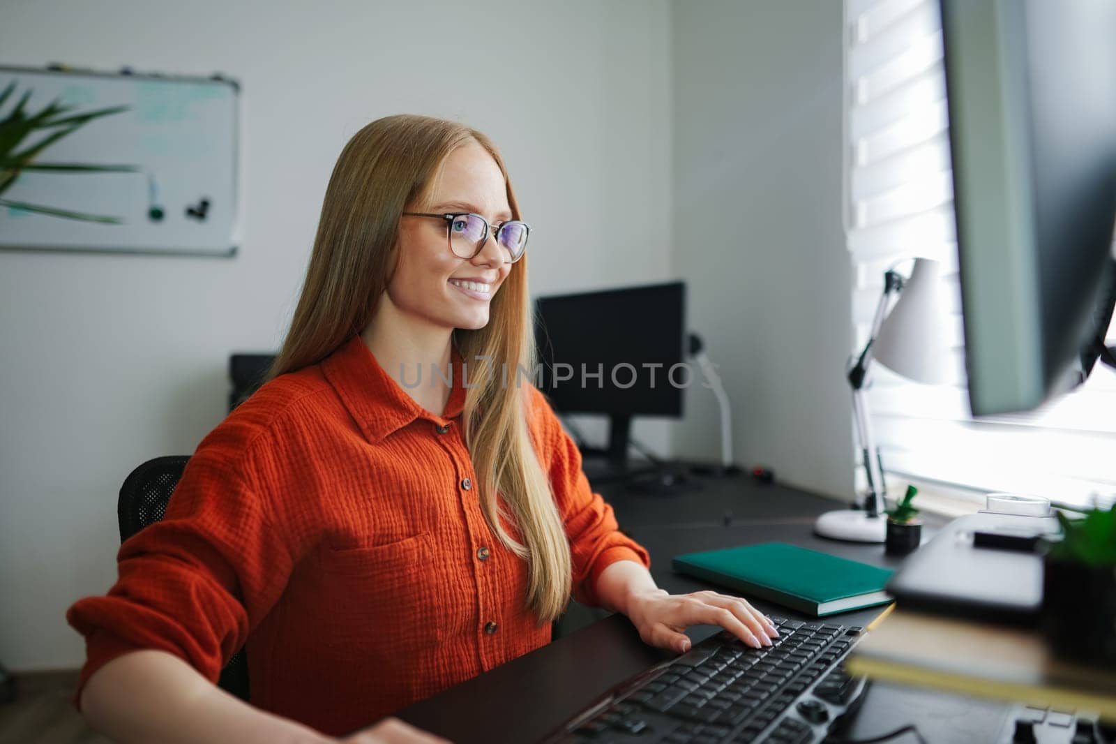 A cheerful woman with long hair works diligently at her desk, enjoying her task.
