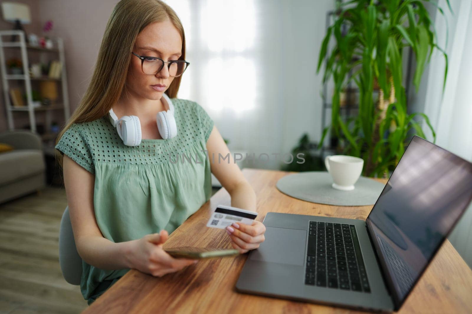 A woman with glasses shops online at a wooden table.
