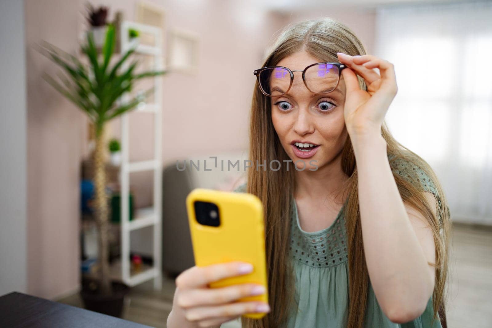 A young woman expresses shock and delight while viewing her phone screen.