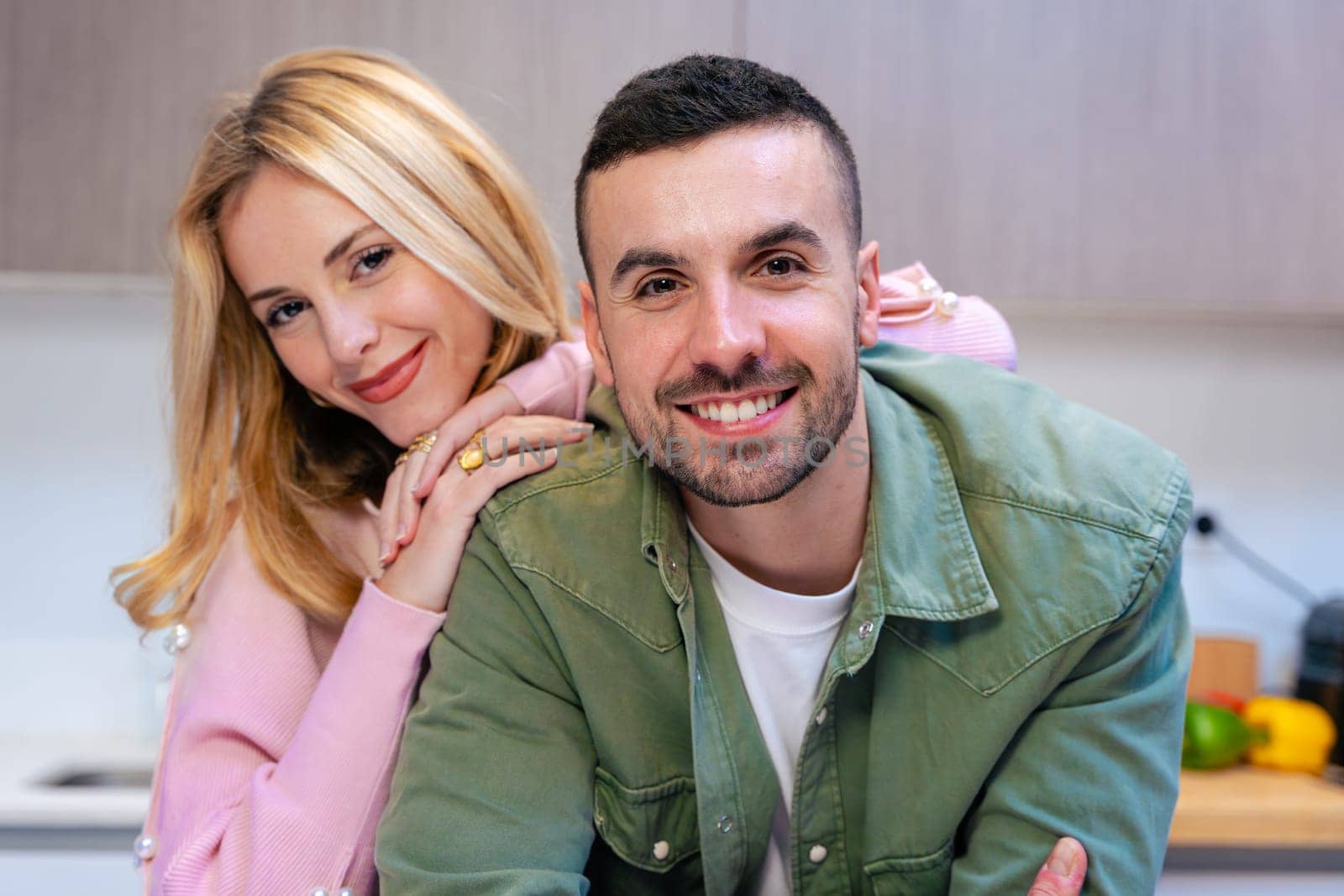 Cheerful young couple smiling warmly at the camera while posing together in a bright and modern kitchen. Their relaxed posture and affectionate expression reflect love, comfort, and connection.