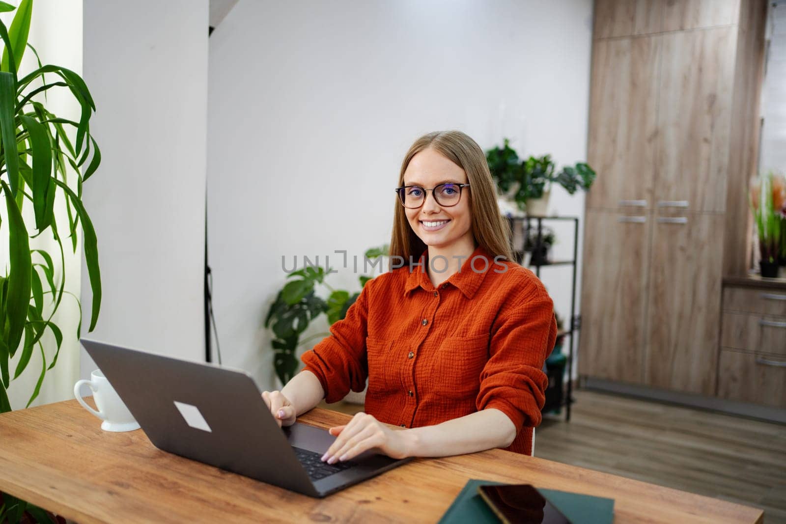 A woman wearing glasses engages with her laptop in a cozy environment.