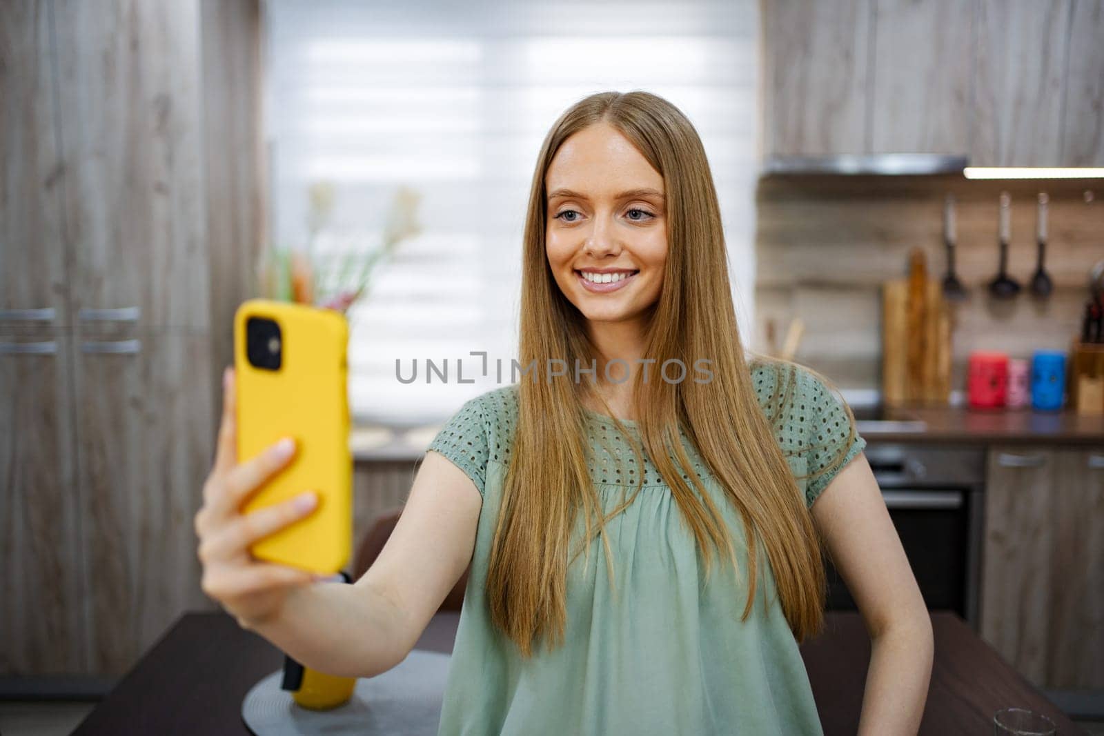 Young woman happily taking a selfie in a stylish kitchen setting.