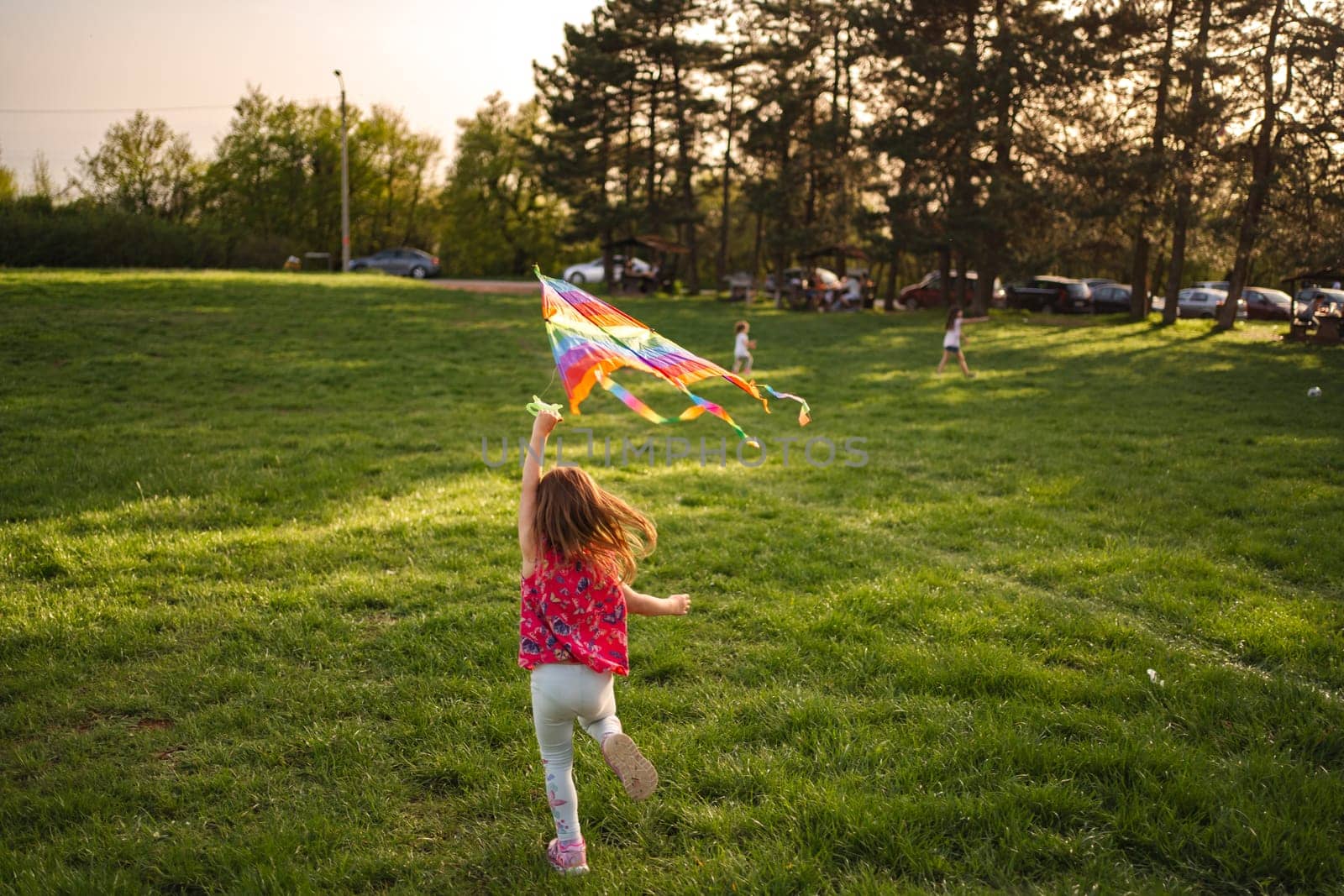 In a vibrant park during golden hour, children race across the lush grass, their laughter filling the air as they fly bright kites that dance in the wind, creating a picturesque moment of joy.