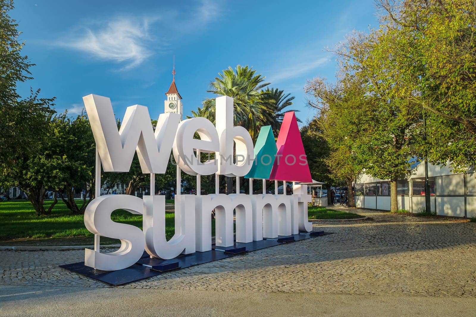Nov 6, 2024 - Lisbon, Portugal: Big Web Summit sign displayed outdoors in park with lush palm trees on sunny day clear blue skies. Major technology conference,internet technology, emerging technology, marketing, AI solution, spirit of innovation