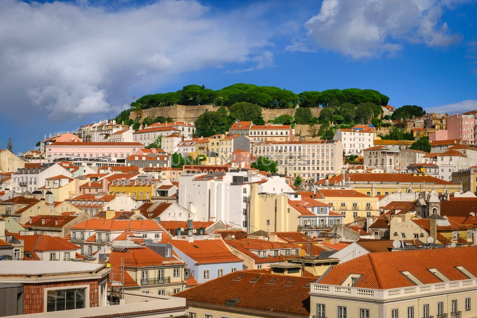 Scenic view of Lisbon, Portugal, historic St George castle on top of hill, traditional Portuguese architecture with red-tiled roofs and colorful houses on sunny day with bright blue sky and some clouds. Famous travel destination, summer vacation