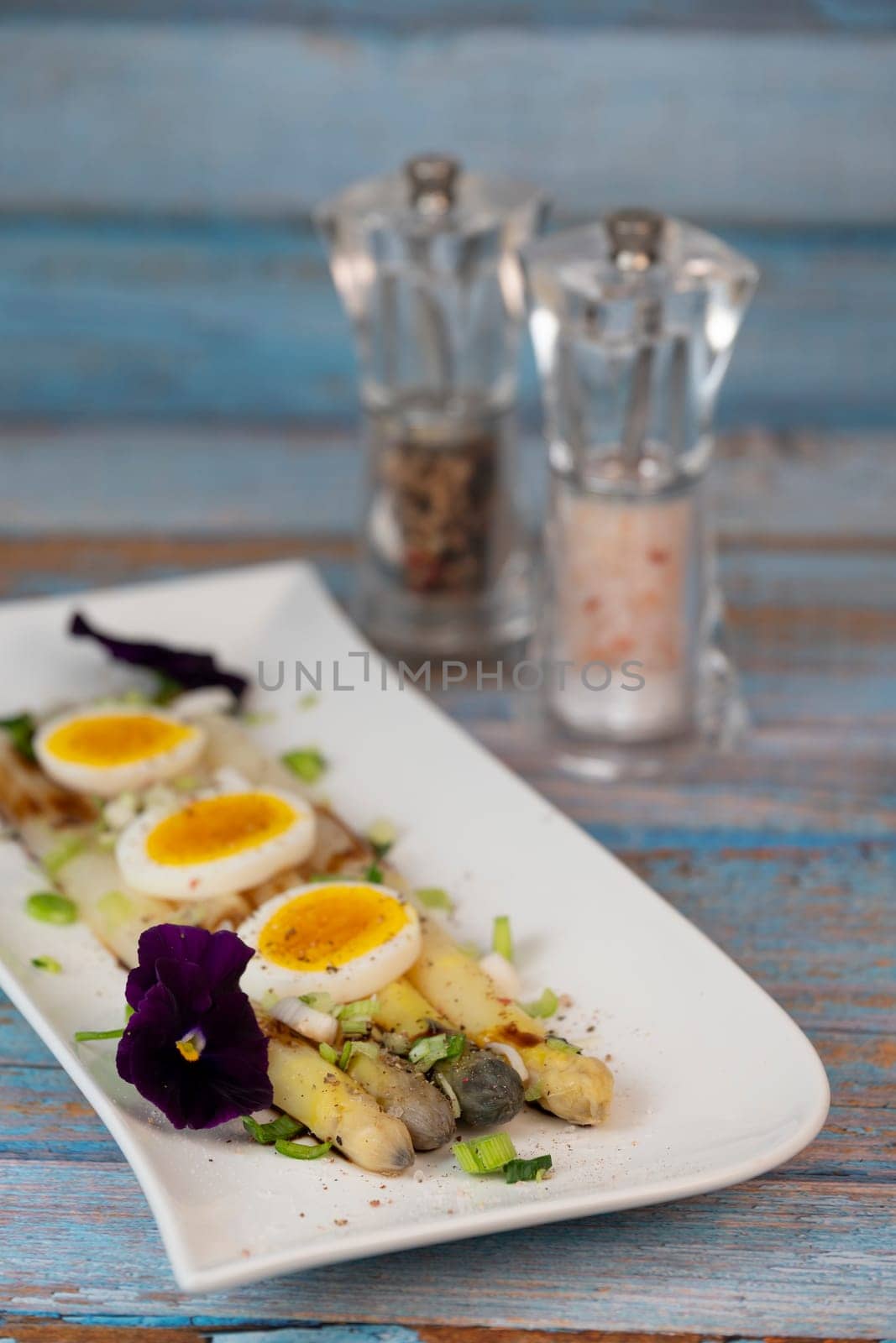 Baked asparagus with boiled egg in big white plate on blue background. High quality photo