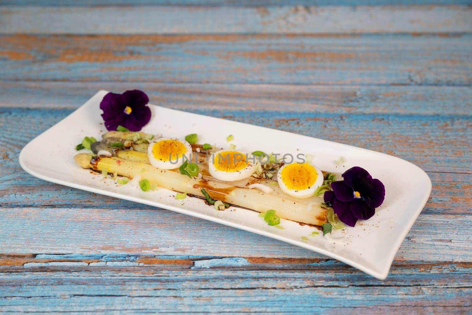 Baked asparagus with boiled egg in big white plate on blue background. High quality photo
