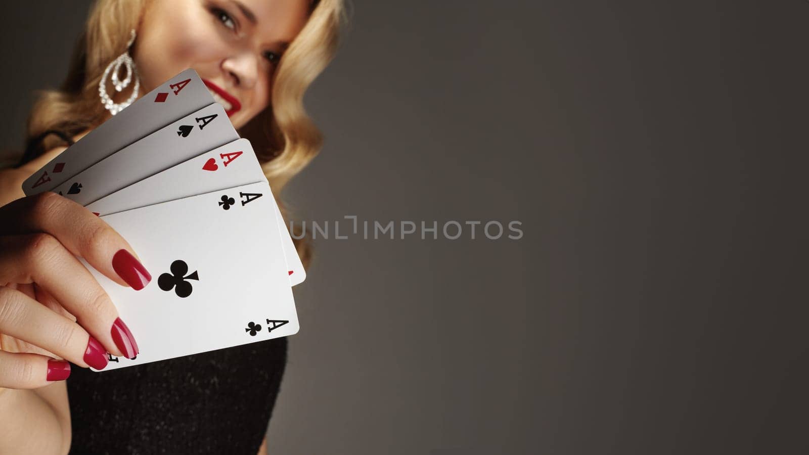 Four aces playing cards in woman's hand. Player with poker quads combination. Elegant female hands with red manicure on nails.