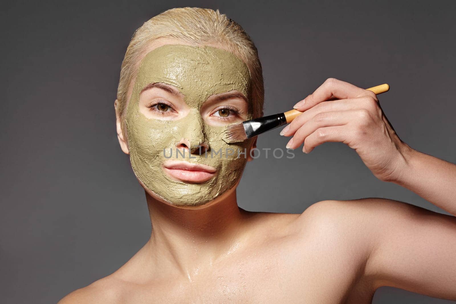 Beautiful Woman Applying Green Facial Mask. Beauty Treatments. Close-up Portrait of Spa Girl Apply Clay Facial mask on grey background.