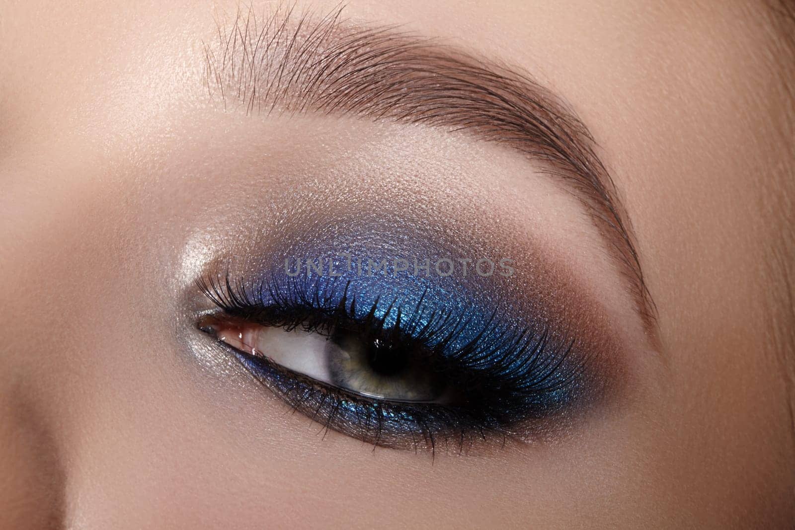 Elegance close-up of female eye with bright dark blue smoky make-up. Macro shot of woman face part. Beauty, cosmetics and makeup