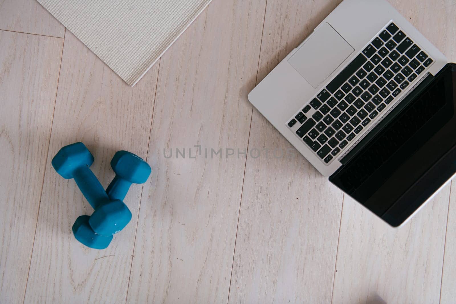 Photo of a laptop, dumbbells and headphones on the floor of the living room. Online training concept