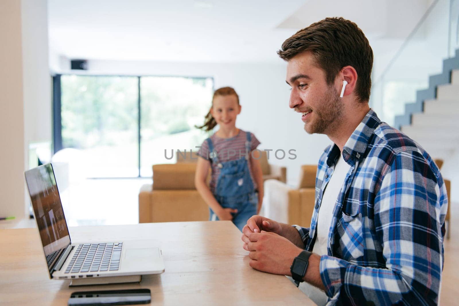 A freelancer sitting at a table in a modern living room, with headphones using a laptop for business video chat, conversation with friends and entertainment.