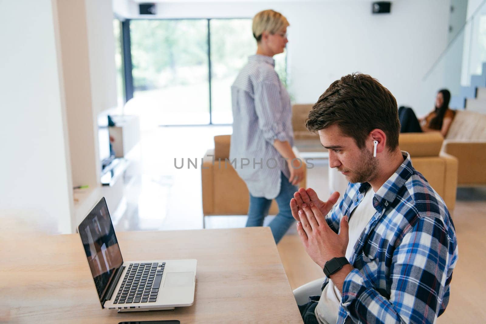 A freelancer sitting at a table in a modern living room, with headphones using a laptop for business video chat, conversation with friends and entertainment.
