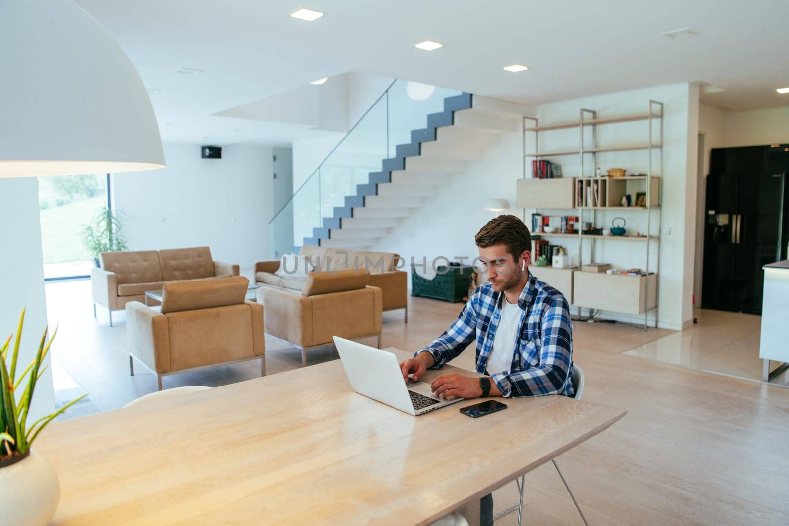 A freelancer sitting at a table in a modern living room, with headphones using a laptop for business video chat, conversation with friends and entertainment.
