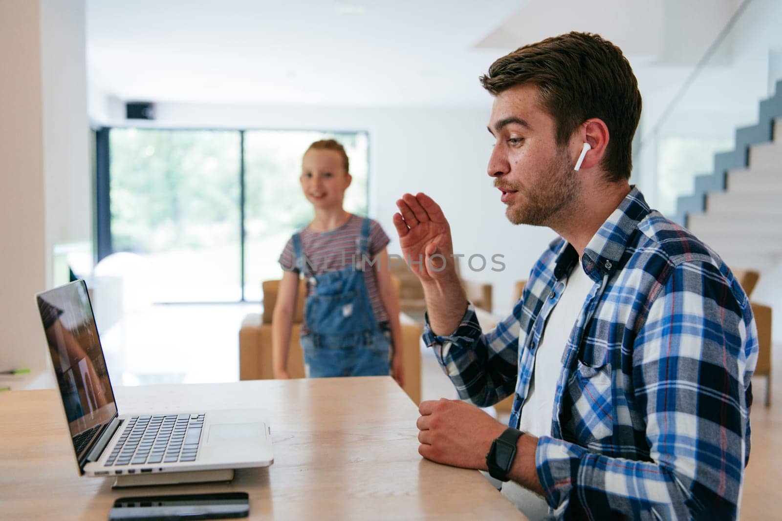 A freelancer sitting at a table in a modern living room, with headphones using a laptop for business video chat, conversation with friends and entertainment.