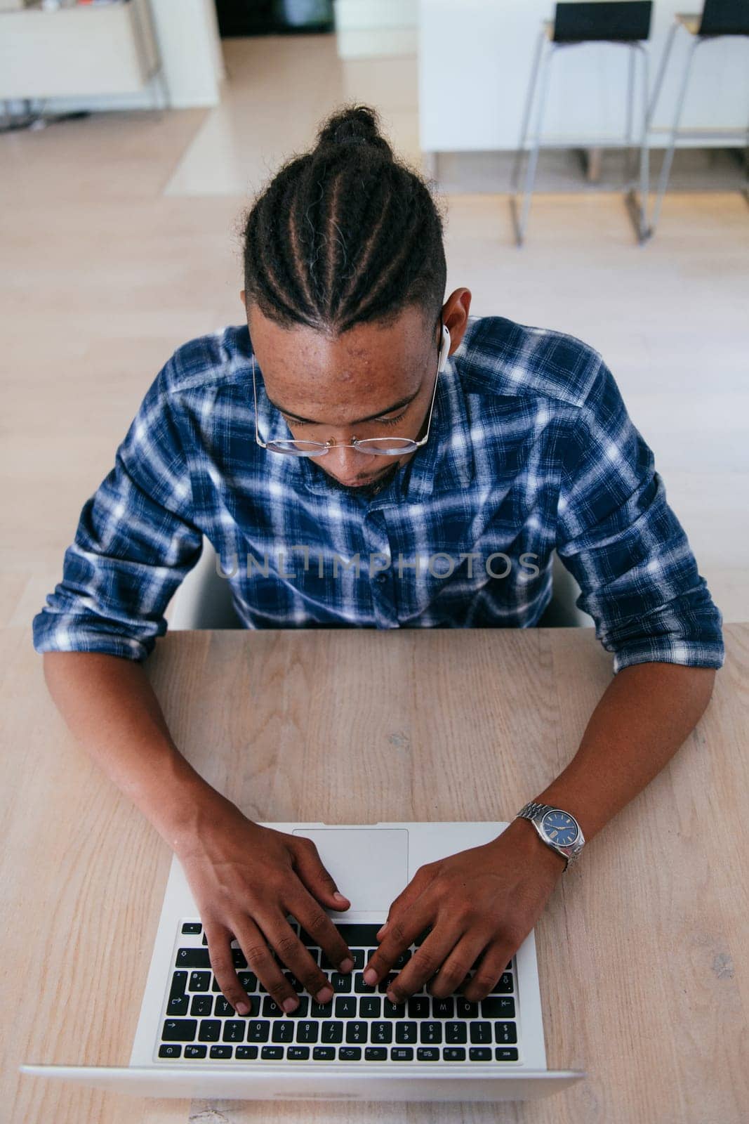 Top view of African American businessman in glasses sitting at a table in a modern living room, using a laptop and smartphone for business video chat, conversation with friends and entertainment.