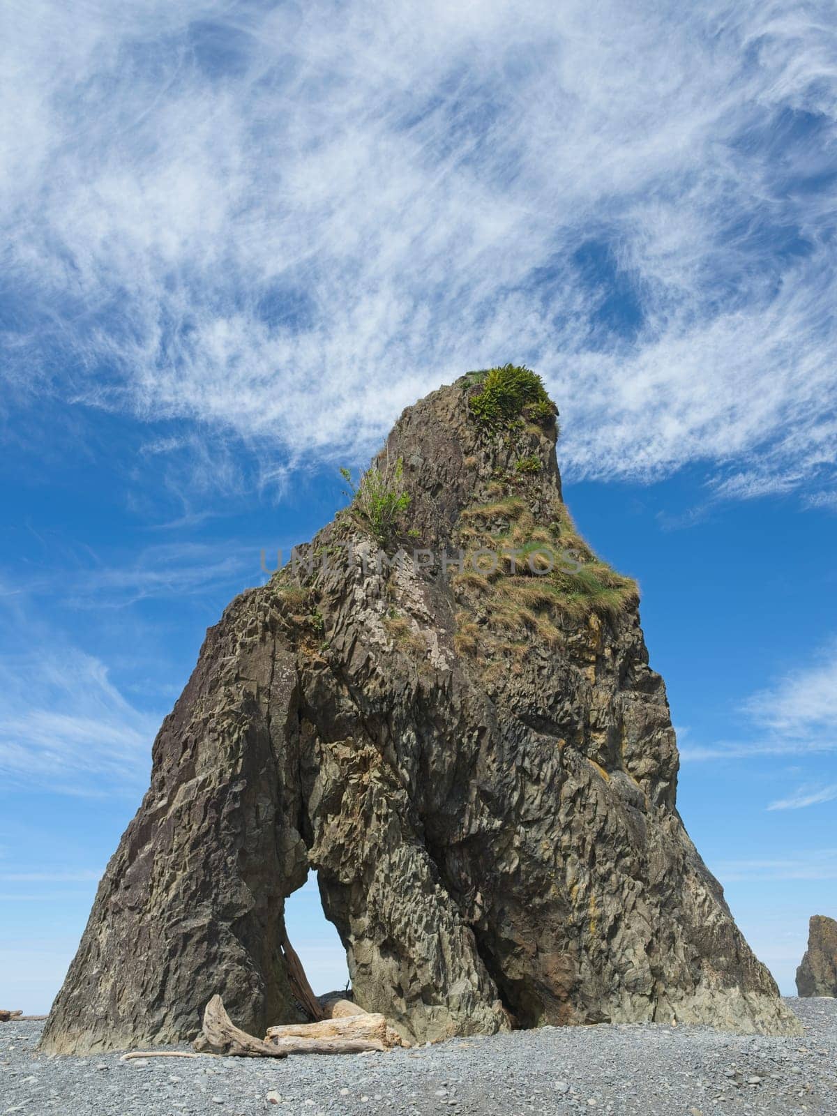 A rock tower under a bright blue sky with a few clouds at Ruby Beach in Washington.