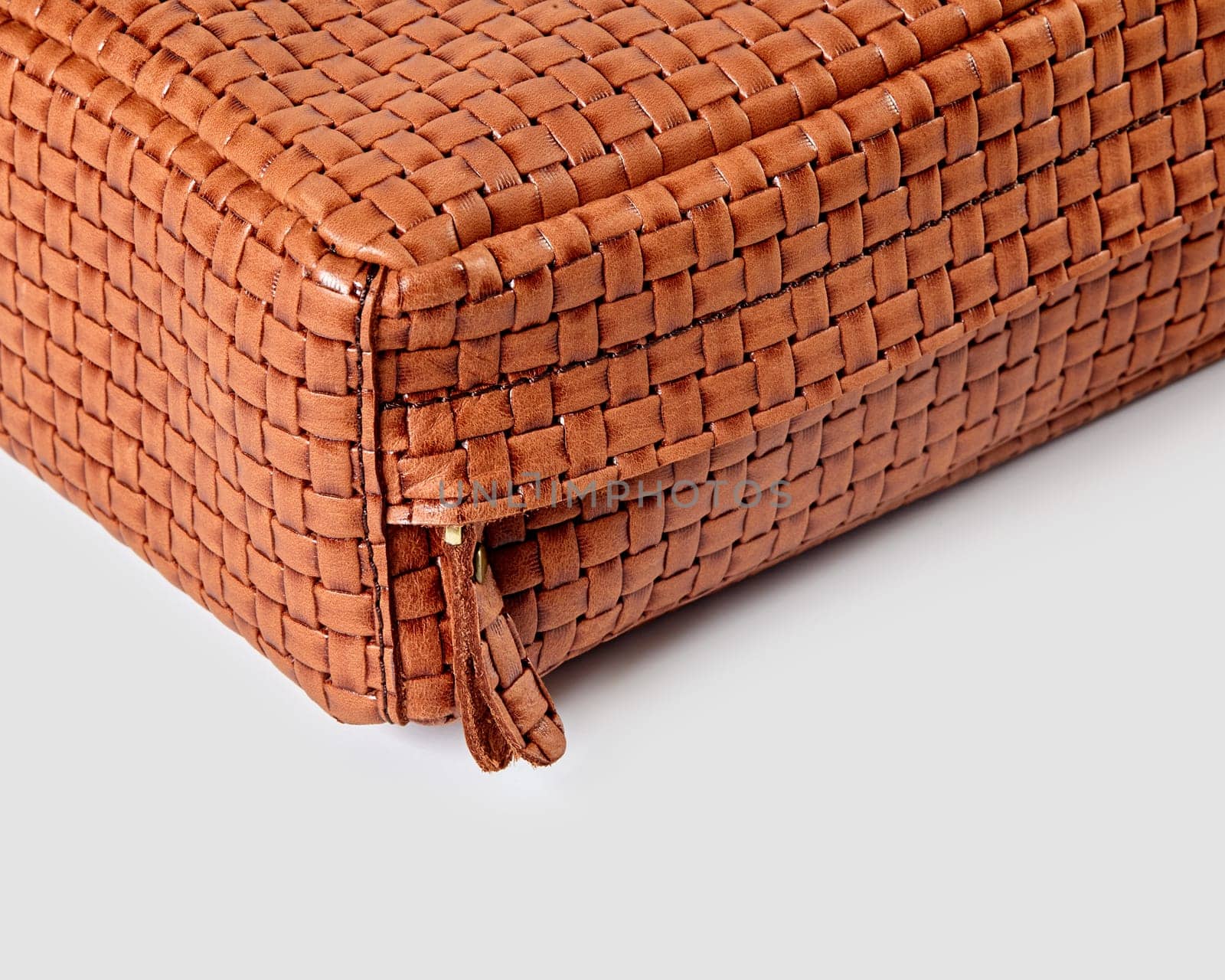 Close-up of the corner of a stylish brown woven leather bag, highlighting the intricate woven pattern and zipper detail