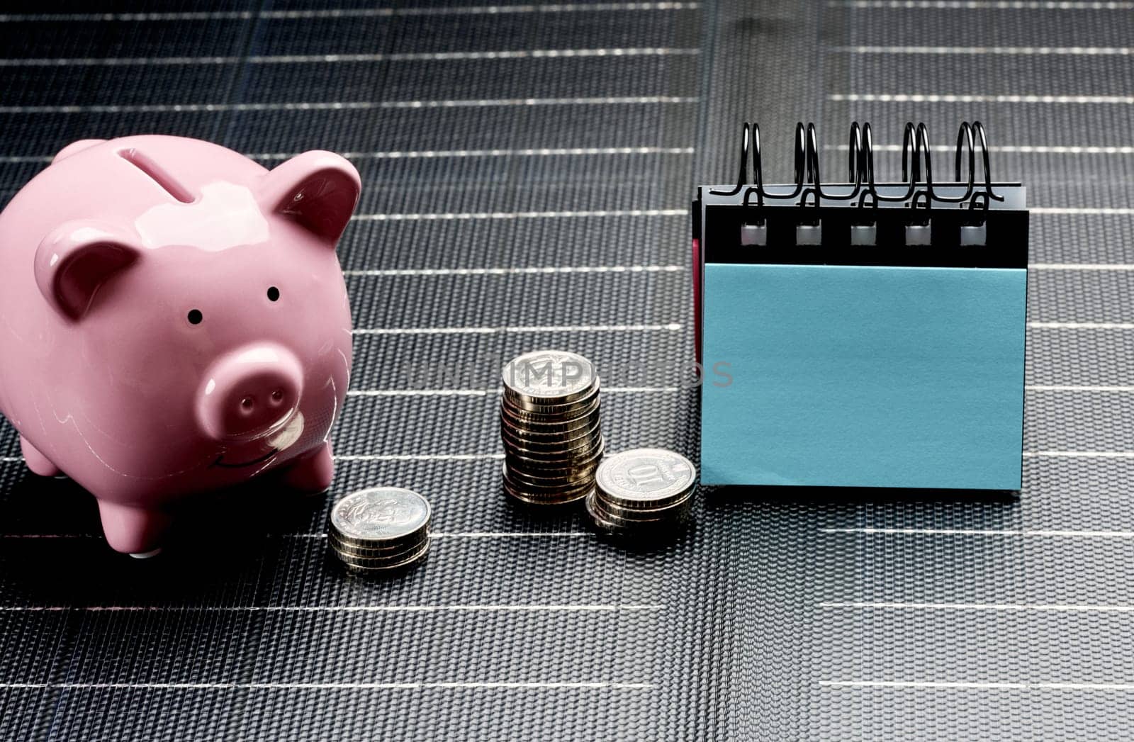 Pink piggy bank next to stacks of coins and desk calendar, symbolizing savings and financial planning, on dark background.
