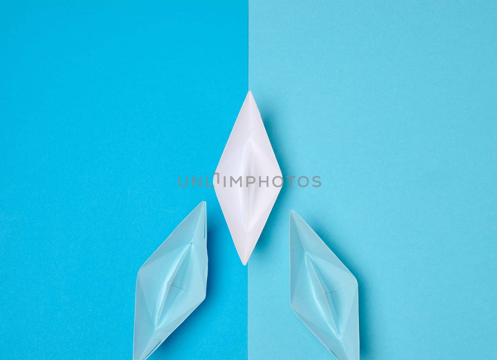A white origami paper boat symbolizing leadership leads two blue boats on a two-tone blue background.