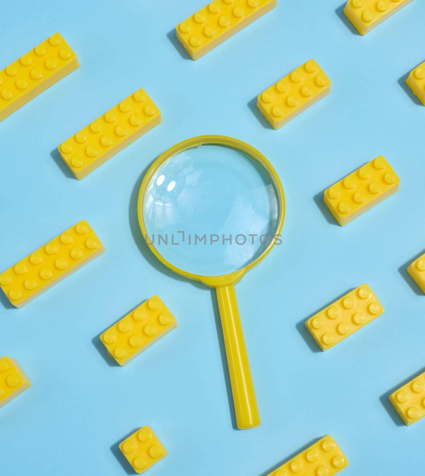 A yellow magnifying glass is surrounded by yellow toy cubes on a blue background.