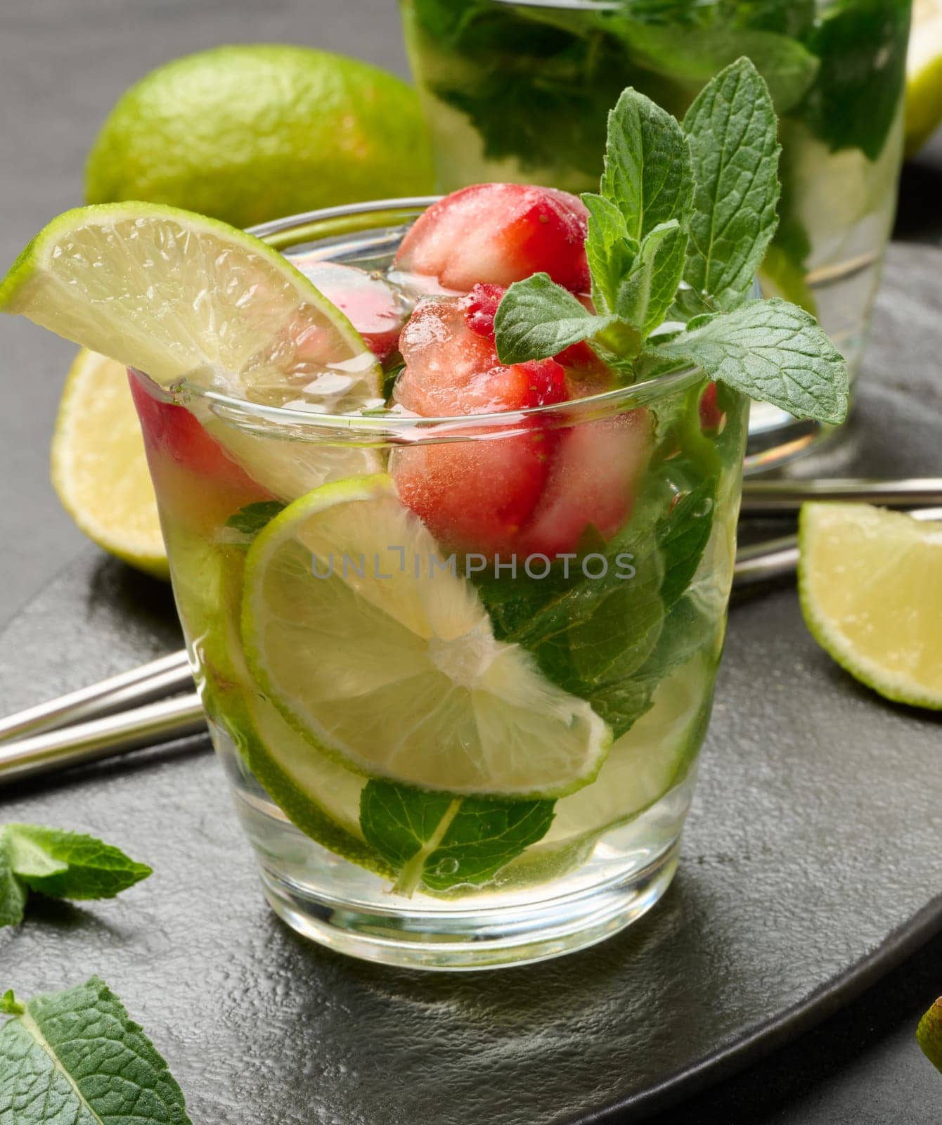 Refreshing mojito cocktail with lime, mint, strawberry, and ice on dark background