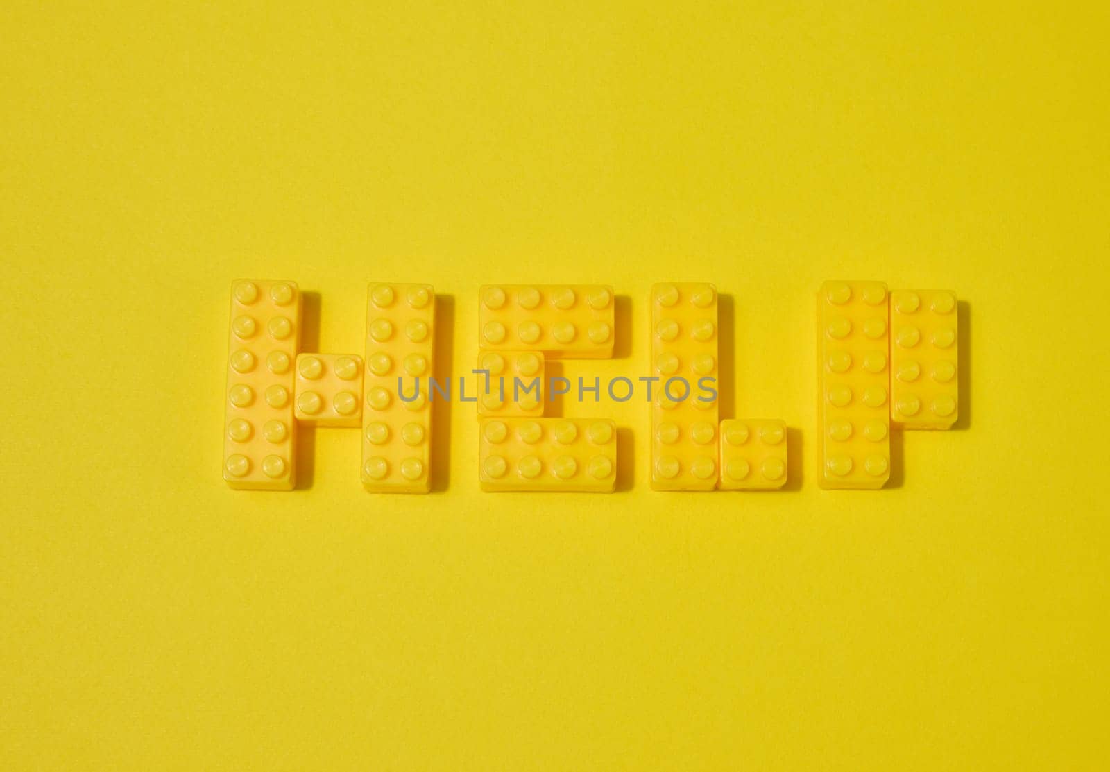 The word HELP, made from yellow toy blocks, is placed on a yellow background