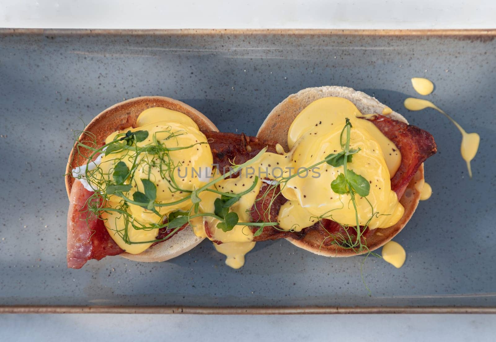 Top view of Eggs Benedict made with english muffin, grilled bacon, a brace of poached hen's eggs & hollandaise sauce and watercress served on ceramic tray. use it as your Wallpaper, Poster and Space for text, Selective focus.