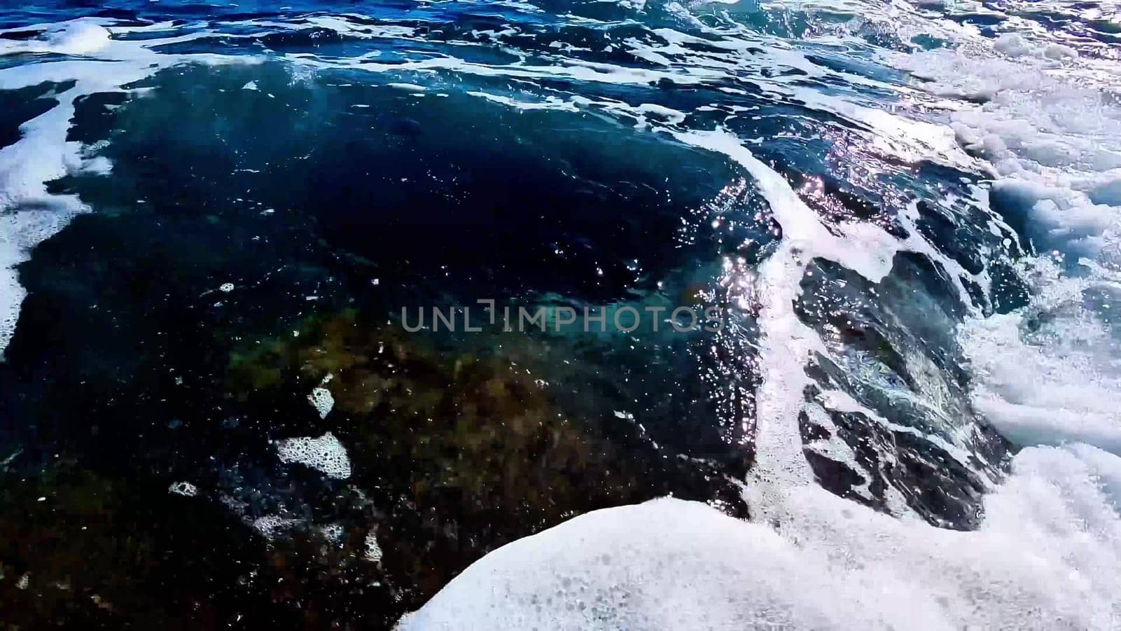The stunning view shows ocean waves crashing against rocks, creating foamy patterns on the rugged terrain