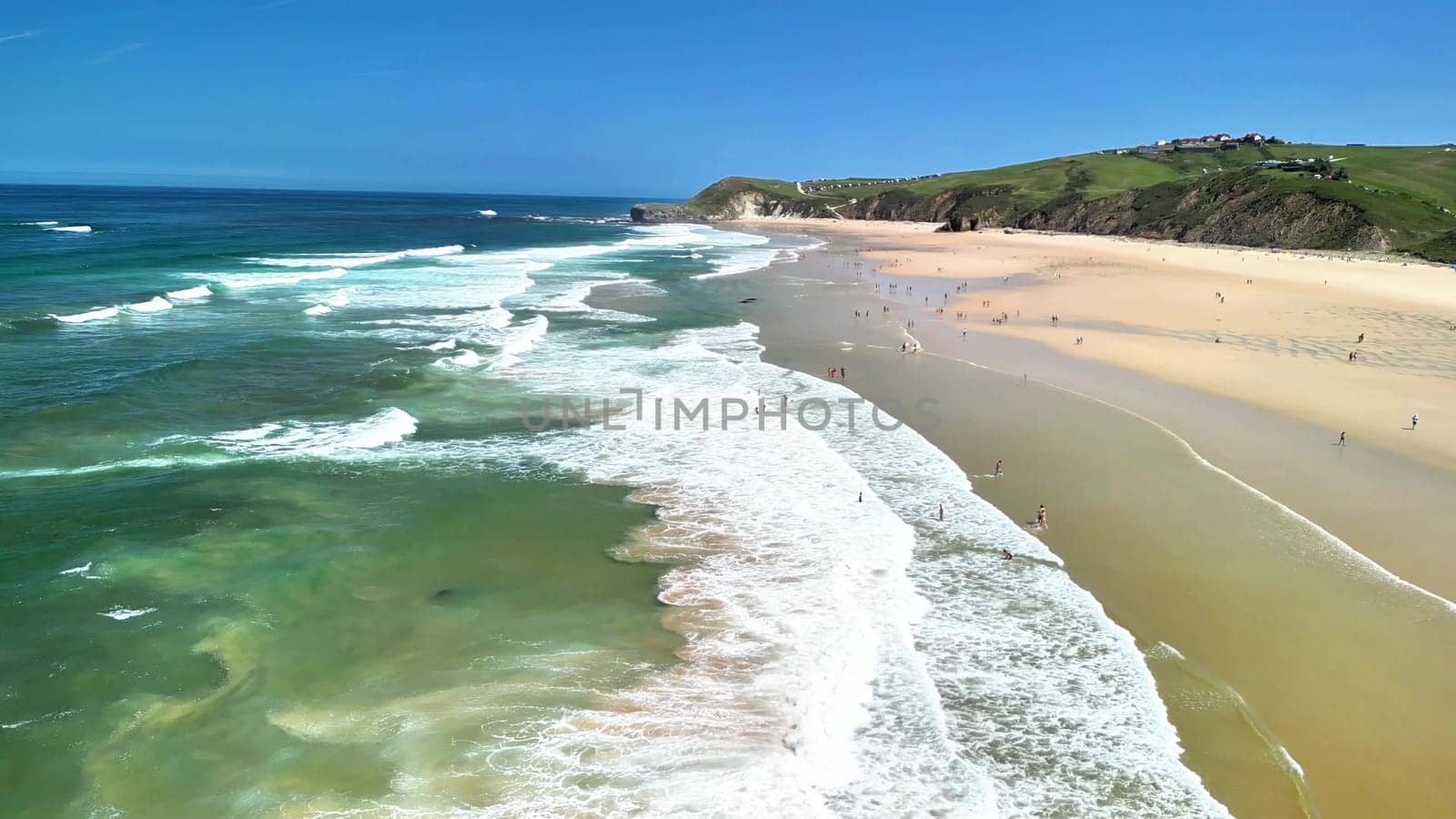 A stunning aerial view showcases a beautiful beach with golden sands and vibrant waves beneath a clear blue sky