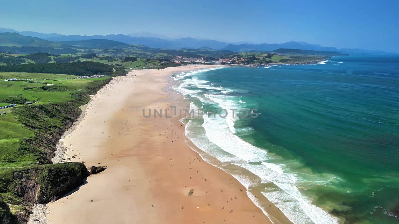 A stunning aerial view of a beautiful beach with clear turquoise waters, waves, and lush greenery nearby