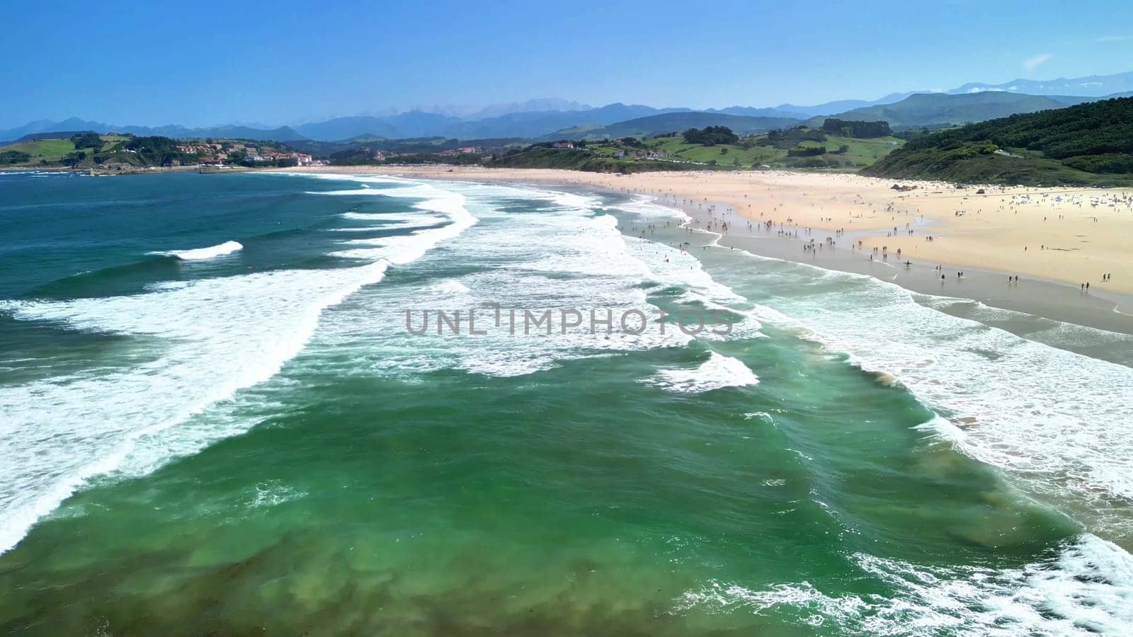 A beautiful and picturesque beach scene with gentle waves, lush green hills, and happy people enjoying the warm sun