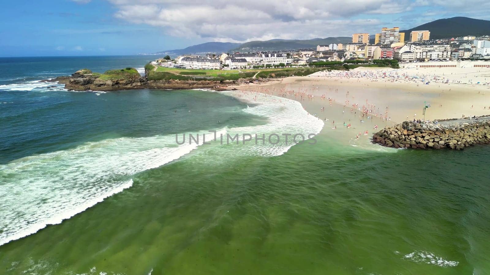 A stunning aerial shot captures a vibrant beach scene, showcasing beautiful waves and beachgoers enjoying the sunny day