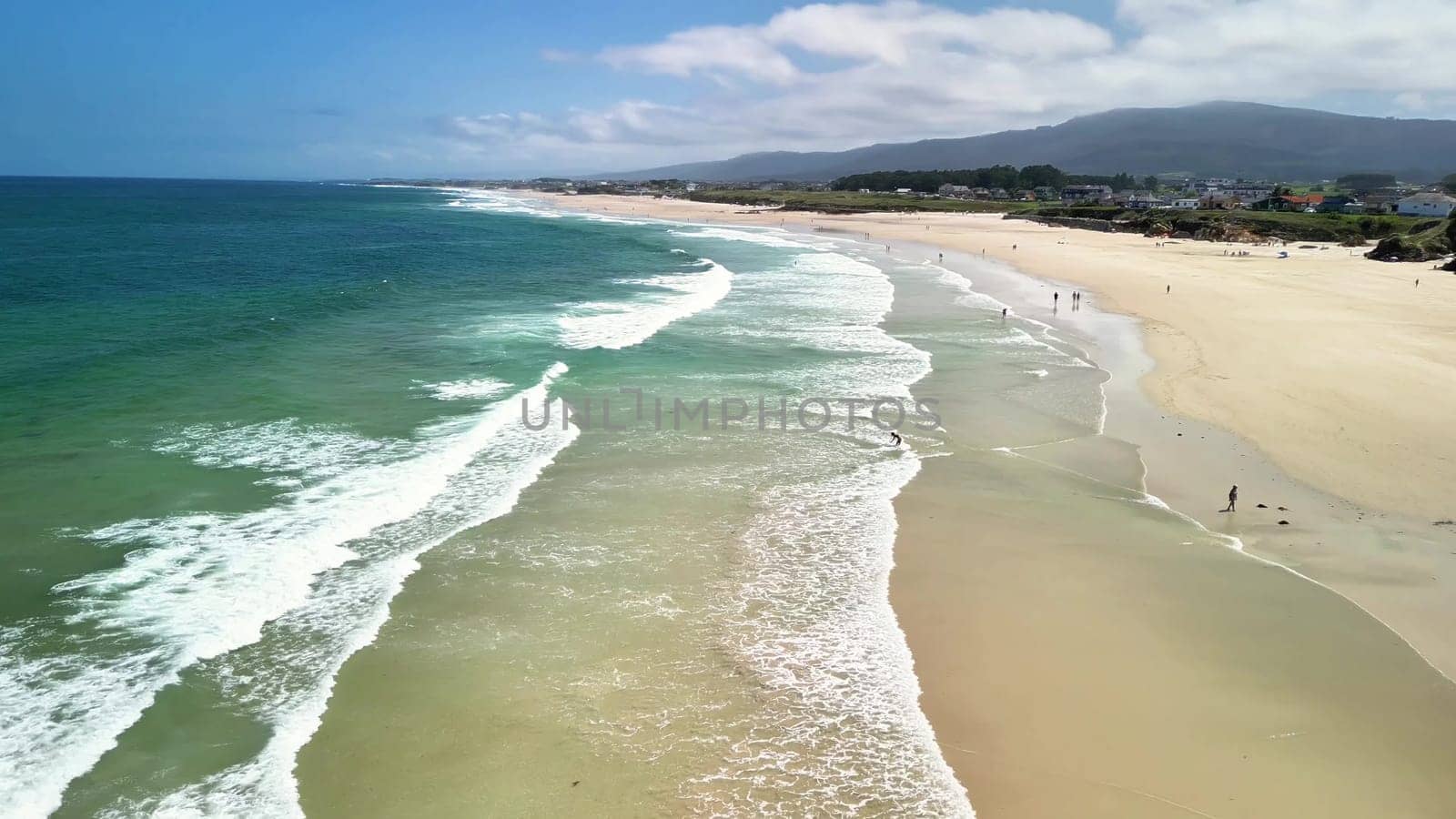 This is a stunning aerial shot of a tranquil beach that features gentle, rolling waves and clear blue skies